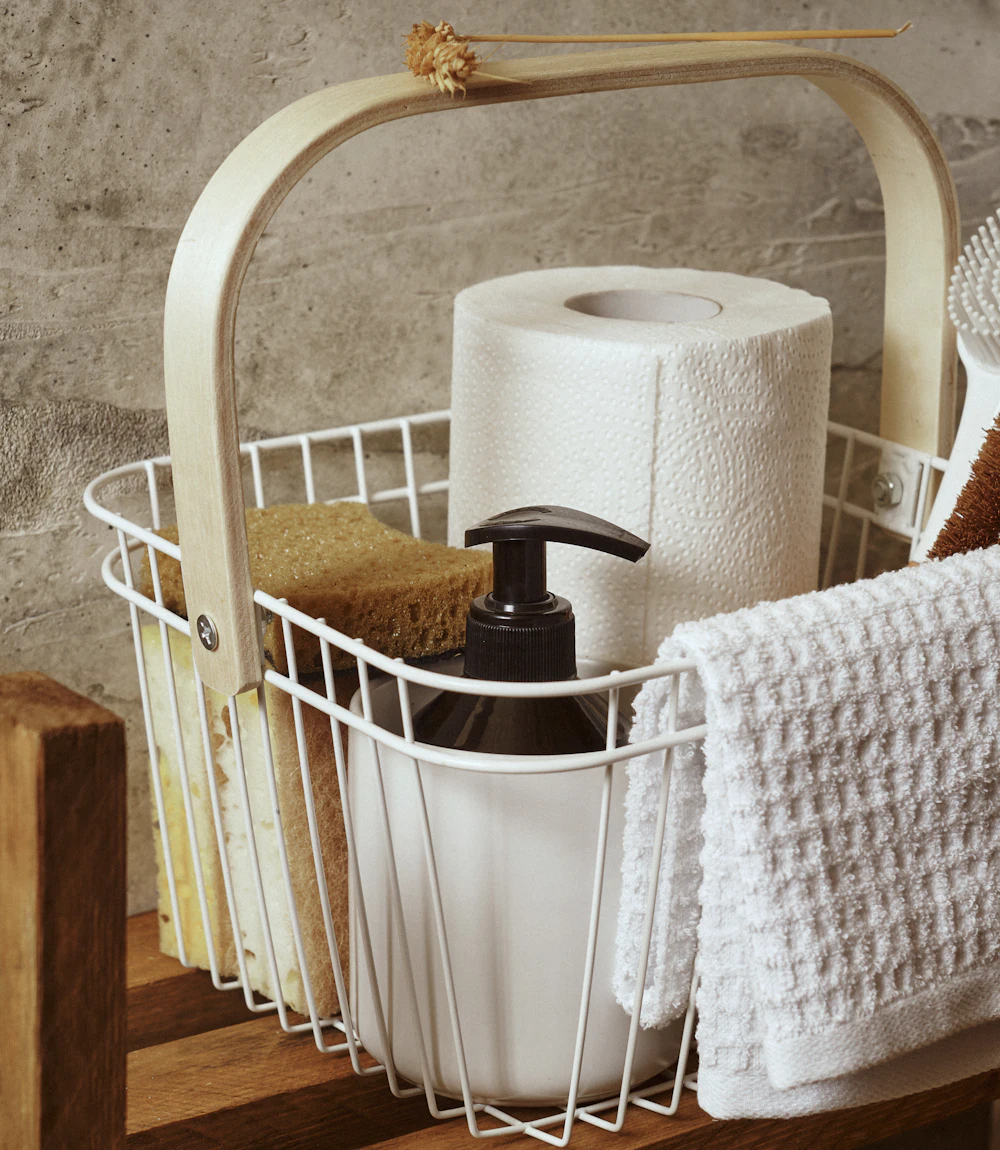 White wire caddy of cleaning supplies on a wooden shelf