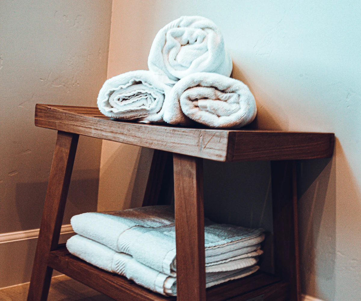 Rolled and folded white towels on a wooden bathroom stool